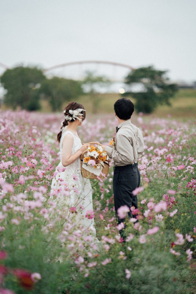 コスモス畑で花かごを持ち景色を眺める新郎新婦