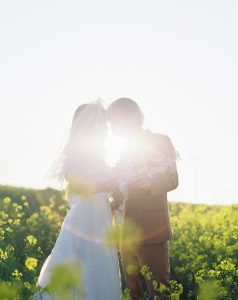 菜の花畑で向かい合う新郎新婦