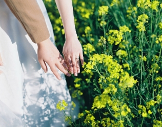 菜の花の中で手をつなぐ新郎新婦