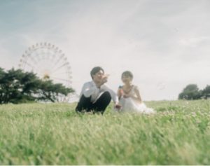 観覧車を背景に芝生に座る新郎新婦