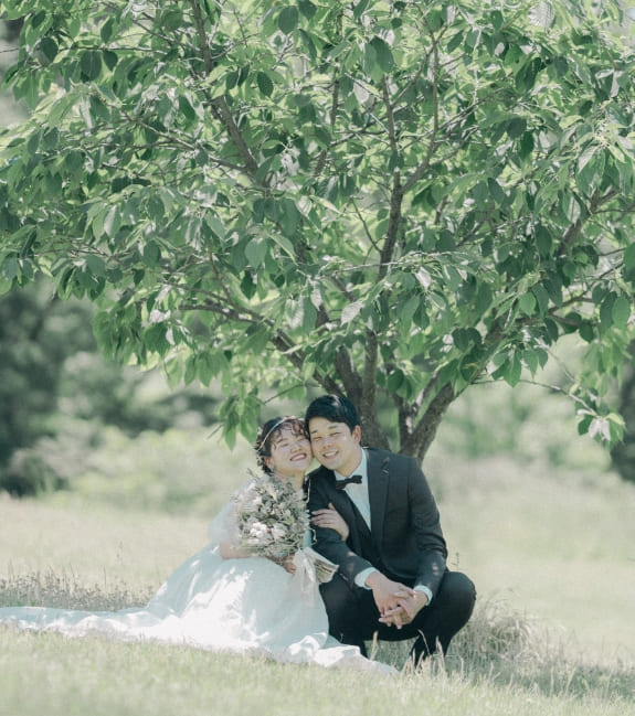 木陰の芝生で笑う新郎新婦