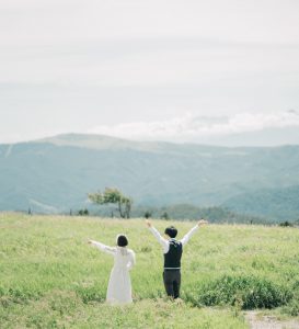 高原で両手を広げる新郎新婦