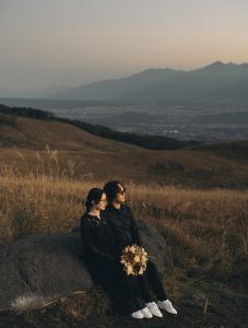 黒い衣装ですすき野原に座る新郎新婦