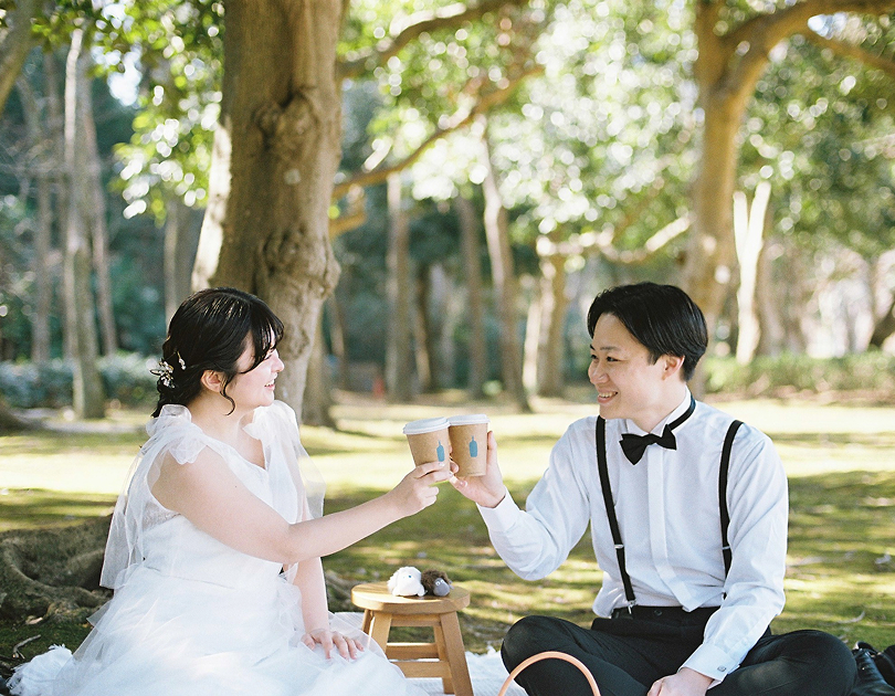 木陰でカップを掲げる新郎新婦