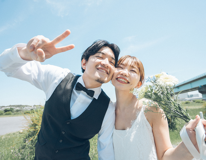 青空の下でピースする新郎新婦