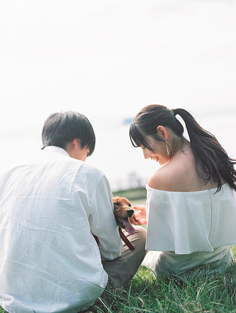 芝生に座る新郎新婦と愛犬の後ろ姿