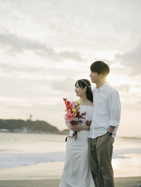 夕暮れの海辺に立つ新郎新婦