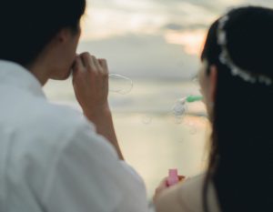 夕暮れの海でシャボン玉を吹く新郎新婦