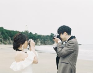 海辺でカメラを向け合う新郎新婦