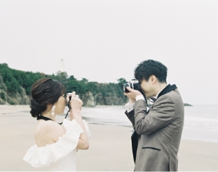 海辺でカメラを向け合う新郎新婦