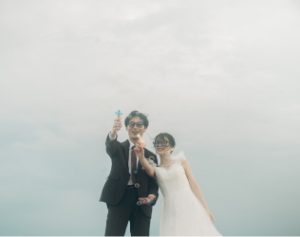 海辺で小物を掲げる新郎新婦