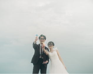 海辺で小物を掲げる新郎新婦