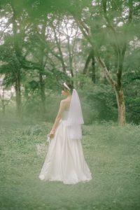 緑の森にたたずむウェディングドレス姿の花嫁