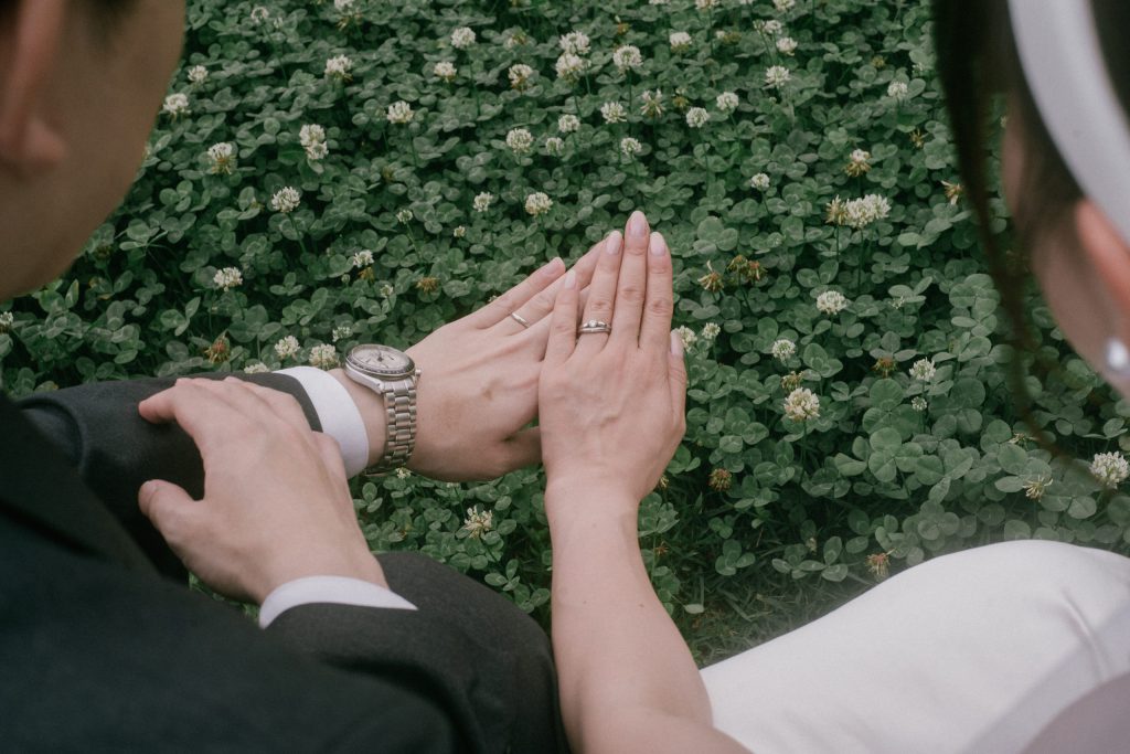 シロツメクサの上で結婚指輪を重ねる新郎新婦の手元