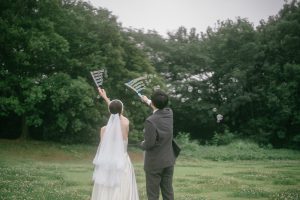 森林公園の芝生でシャボン玉を飛ばす新郎新婦