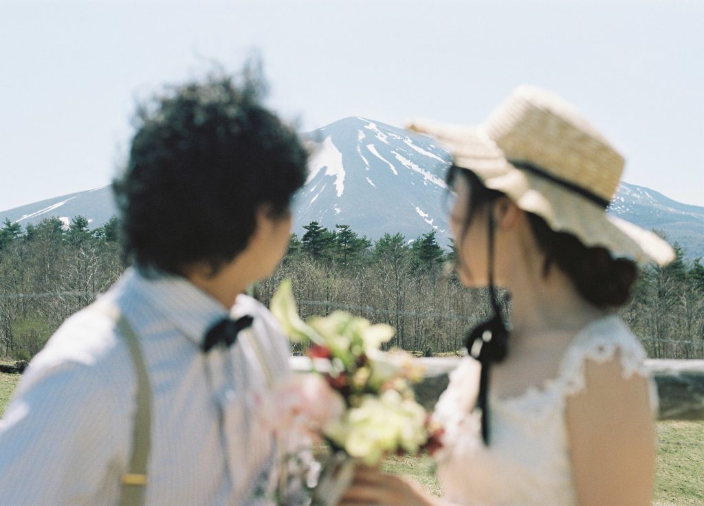 麦わら帽子をかぶり山を背に寄り添う新郎新婦