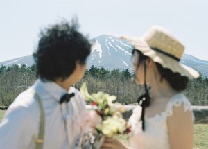 麦わら帽子をかぶり山を背に寄り添う新郎新婦