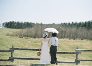牧場の柵越しに山並みを眺める新郎新婦の後ろ姿