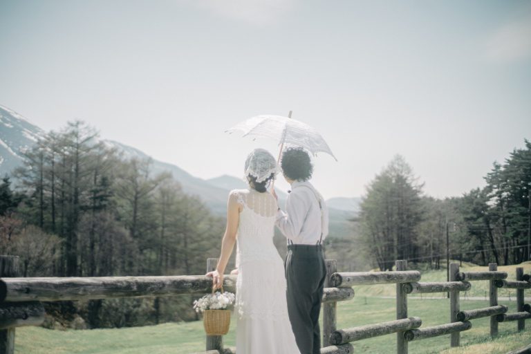 白い日傘をさし柵の前に立つ新郎新婦の後ろ姿