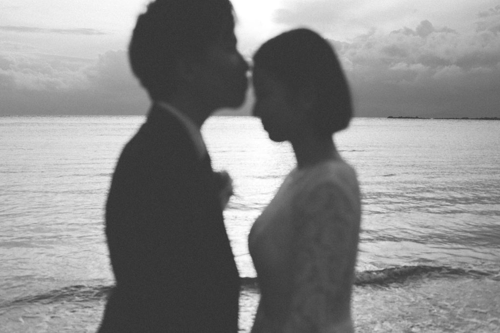 夕暮れの海を背に見つめ合う新郎新婦のシルエット