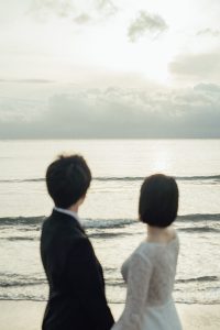 波打ち際で寄り添い海を眺める新郎新婦の後ろ姿