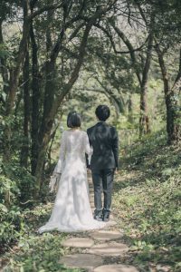 新緑の小道を手をつないで歩く新郎新婦の後ろ姿