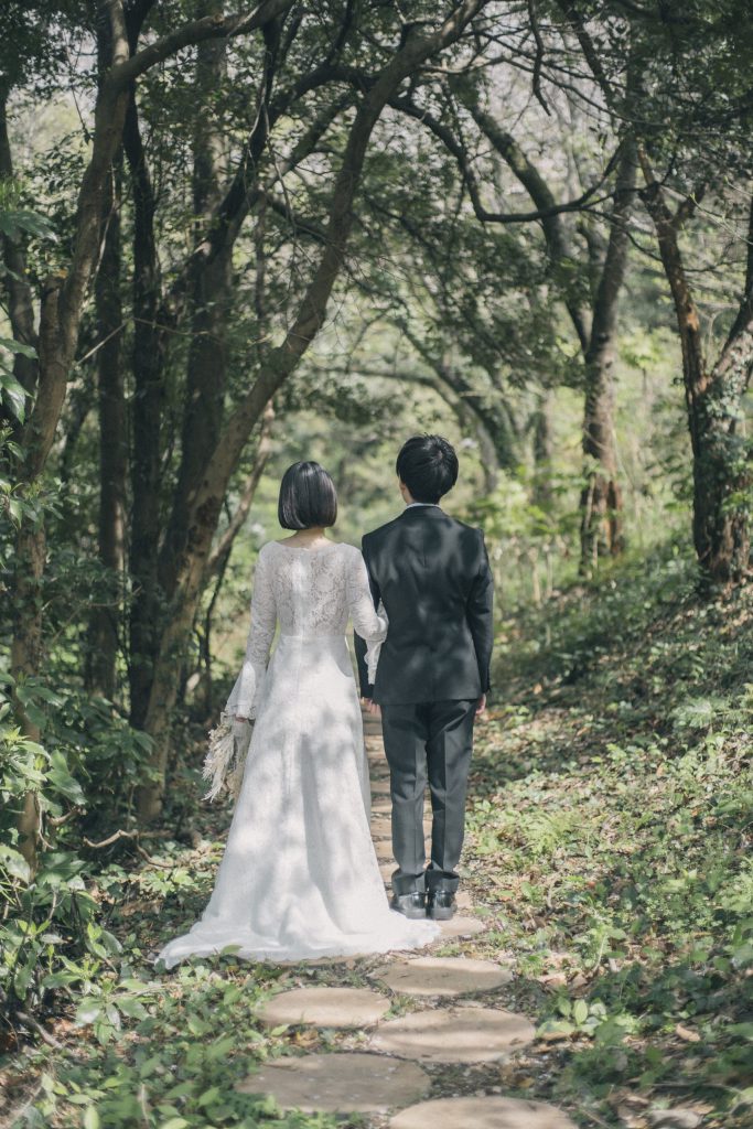 新緑の小道を手をつないで歩く新郎新婦の後ろ姿
