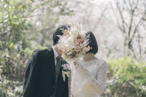 桜の下でブーケ越しに顔を寄せる新郎新婦