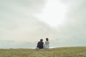 広い空と海を背景に座る新郎新婦の遠景