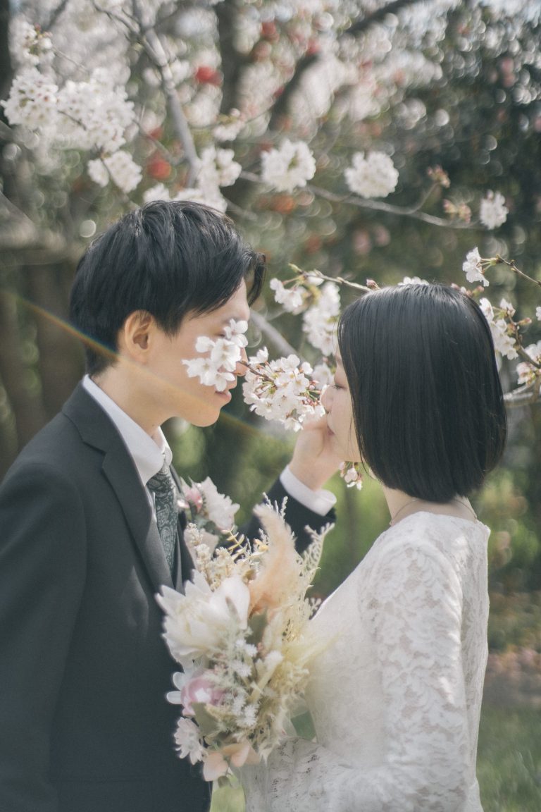 満開の桜の下で鼻先を寄せ合う新郎新婦