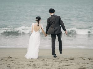波打ち際を手をつないで歩く新郎新婦の後ろ姿