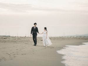 海辺を並んで歩く新郎新婦の後ろ姿