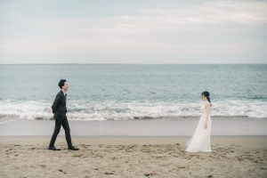 笑顔で見つめ合いながら浜辺を歩く新郎新婦