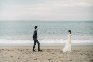 花束を後ろ手に隠しながら花嫁に近づく新郎
