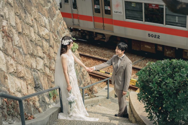 電車が走る石段でしゃがみ手をつなぐ新郎新婦