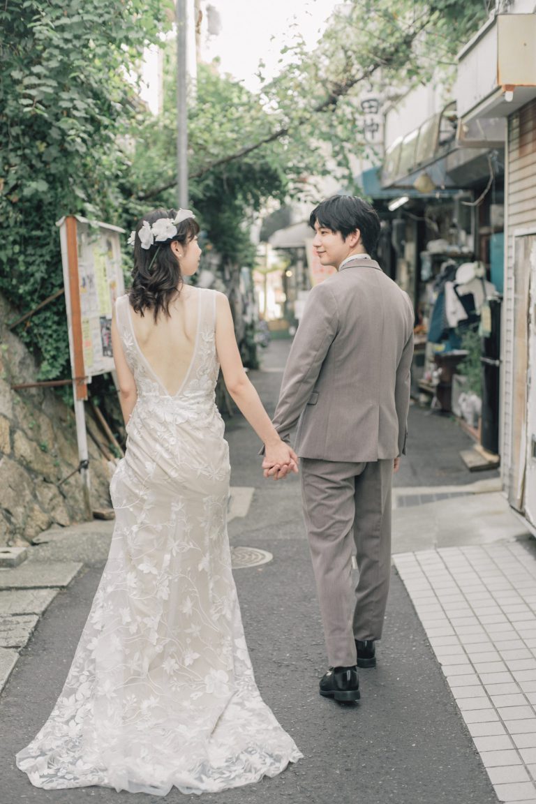 商店街の路地を手をつないで歩く新郎新婦の後ろ姿